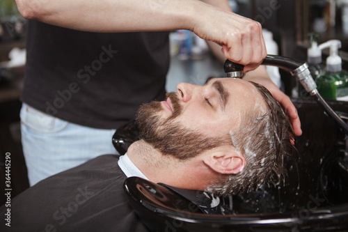 Bearded man enjoying hair wash by professional barber at the salon