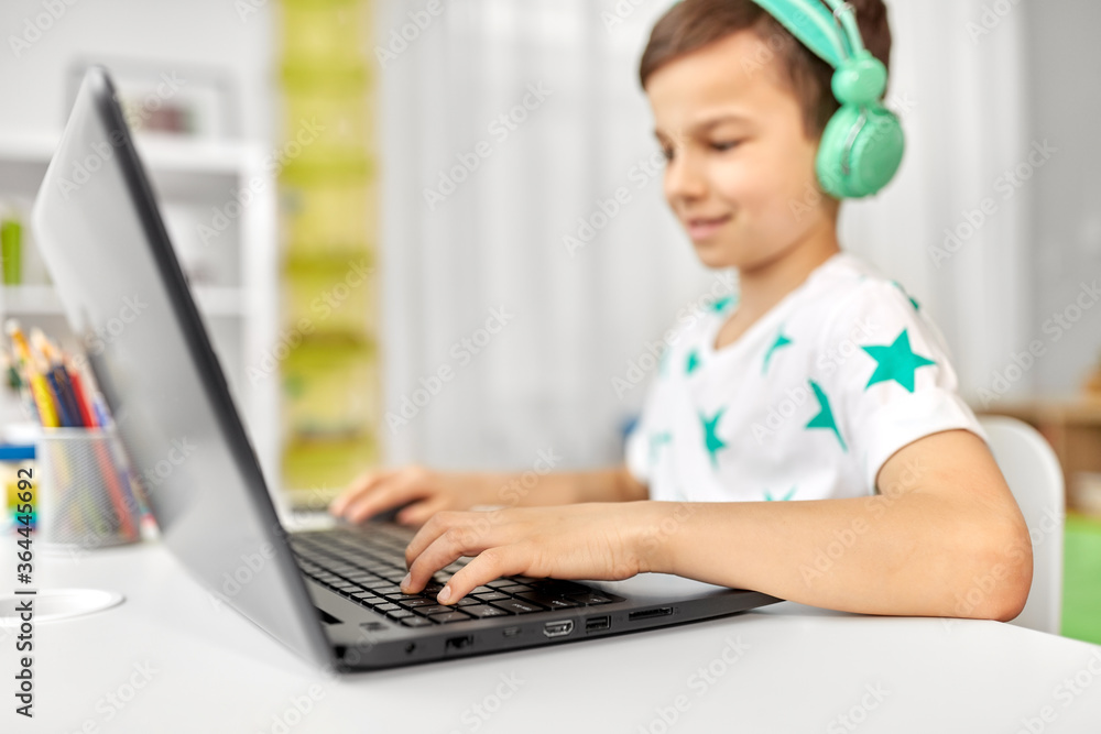 technology, gaming and people concept - boy in headphones playing video game on laptop computer at home technology, gaming and people concept - boy in headphones playing video game on laptop computer at home