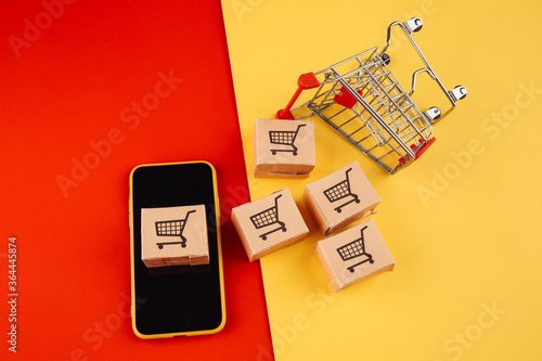 Paper brown boxes on smartphone and trolley isolate on colorful background. The concept of delivery of goods from the online store to the house.