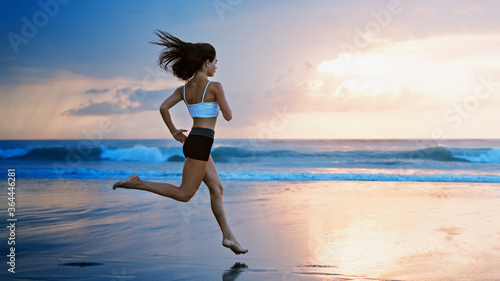 Barefoot young girl with slim body running along sea surf by water pool to keep fit and burning fat. Beach background with blue sky. Woman fitness, jogging sports activity on summer family vacation.