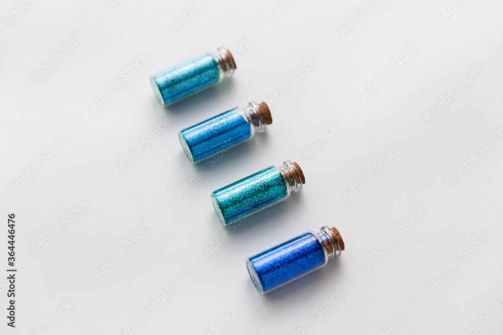 Naklejka premium party, decoration and holidays concept - glitters of different blue shades in small glass bottles with cork stoppers over white background