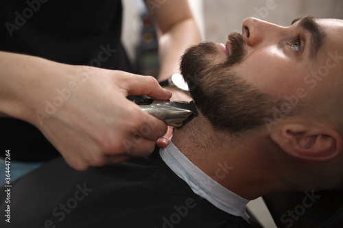 Cropped close up of a bearded handsome man relaxing at barbershop while barber trimming his beard