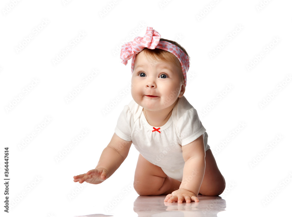 Curios much surprised adorable infant baby girl in white body and hair bow decoration creeps on floor looking at camera Curios much surprised adorable infant baby girl in white body and hair bow decoration creeps on floor looking at camera