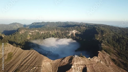 A drone capture of an early morning over the Kelimutu Lakes on Flores, Indonesia. The volcanic lakes are located in volcanic craters. One of the lakes is covered with fog. Golden hour. Calmness
