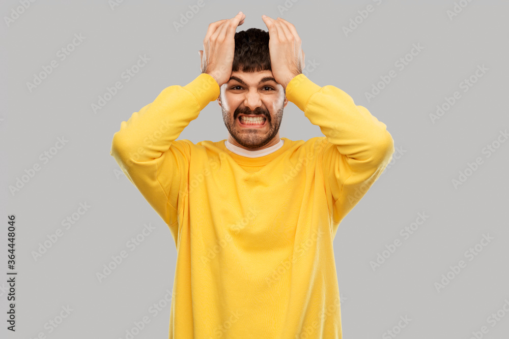 stress, emotions and people concept - angry young man in yellow sweatshirt holding to head over grey background stress, emotions and people concept - angry young man in yellow sweatshirt holding to head over grey background