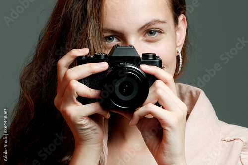 A girl photographer in a pink jacket holds a mirrorless camera in her hands. © Oleg Samoylov