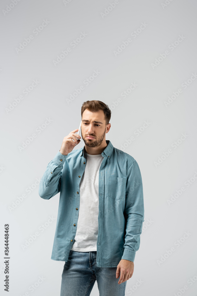 sad young man talking on smartphone isolated on grey sad young man talking on smartphone isolated on grey