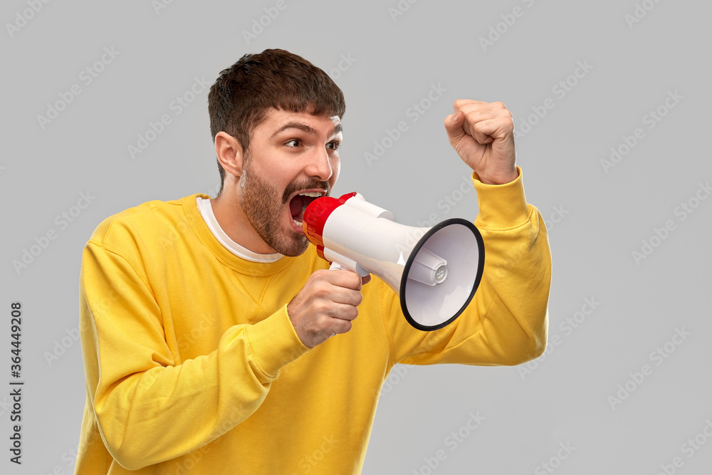 communication and people concept - angry young man in yellow sweatshirt shouting to megaphone over grey background communication and people concept - angry young man in yellow sweatshirt shouting to megaphone over grey background