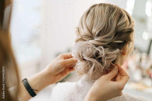 Close-up of hands of hairdresser making hairstyle unrecognizable young blonde woman in beauty salon  back view. Concept of beauty  fashion and stylish makeup.