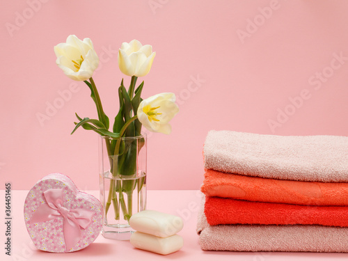 Bouquet of yellow tulips in vase with towels on a pink background.
