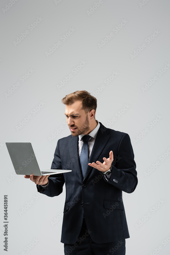 angry handsome businessman in suit using laptop isolated on grey