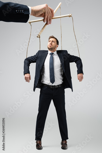 cropped view of puppeteer holding businessman marionette on strings isolated on grey photo