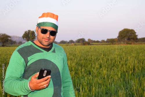 Wearing a tricolor turban, an Indian farmer is talking on his mobile in the evening in his wheat fields, with glasses © Tofan