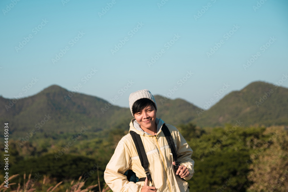 Smiling Asian young man in Long-sleeved shirt and grey hat hiking standing at mountain peak above clouds  Hiker outdoor. Maetip Reservoir Lamphun Province, Northern Thailand Province in the morning.