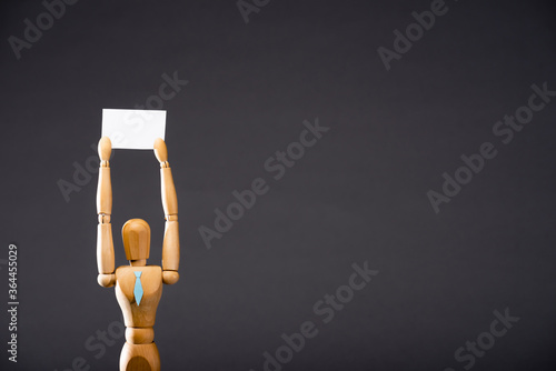 wooden marionette in tie holding blank placard on black background photo