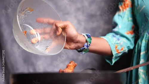 Closeup of the hand of a female chef dropping hot chicken wings from a glass bowl into a frying pan