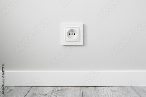 New electrical socket isolated on gray wall. Renovated studio apartment power supply background. Gray wooden floor. Empty copy space white plastic power outlet. photo