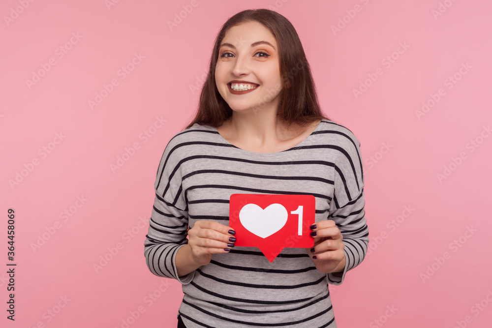 Click Like and follow my blog! Portrait of happy blogger woman in striped sweatshirt holding social media Heart button and looking at camera with toothy smile. studio shot isolated on pink background Click Like and follow my blog! Portrait of happy blogger woman in striped sweatshirt holding social media Heart button and looking at camera with toothy smile. studio shot isolated on pink background