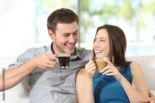 Happy couple with coffee cups looking each other at home