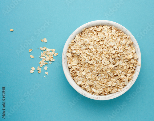 Canvas Print raw oatmeal in a white wooden bowl on a blue background