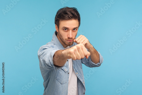 Canvas Print Portrait of man in worker denim shirt standing with boxing gesture, punching to camera, provoking fight or ready to self-defense, struggle concept