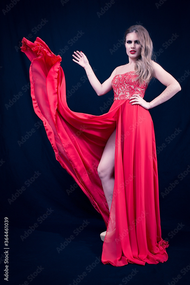 Young Blonde With a Red Silky Dress, That is Flying, Looking Straight, on Deep Blue Background. Fashion Position Young Blonde With a Red Silky Dress, That is Flying, Looking Straight, on Deep Blue Background. Fashion Position
