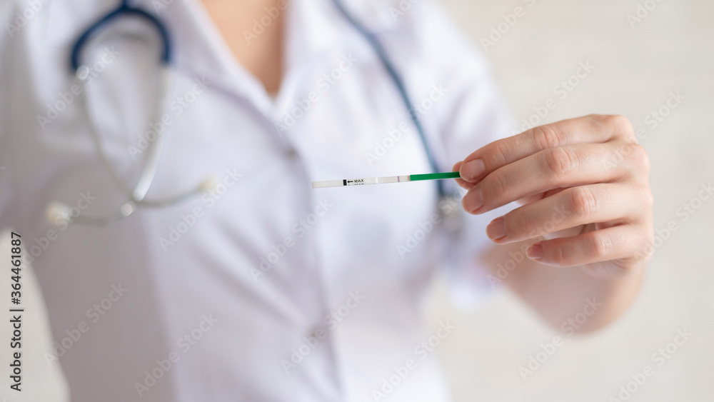 A faceless female doctor holds a negative quick pregnancy test. Gynecologist in a medical coat and with a stethoscope. Problems conceiving a baby. A faceless female doctor holds a negative quick pregnancy test. Gynecologist in a medical coat and with a stethoscope. Problems conceiving a baby.