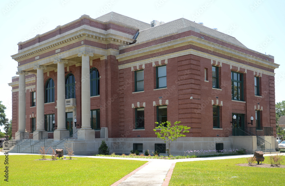 A fine example of a neo-classical, red brick and concrete building, constructed and used as the county courthouse. There are neat lawns and pedestrian access in the foreground.
