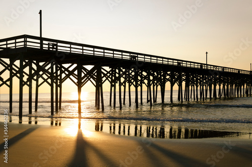 Looking east into a golden sunrise with Pawleys Island pier in silhouette against the bright sun, casting long shadows on the sand. photo