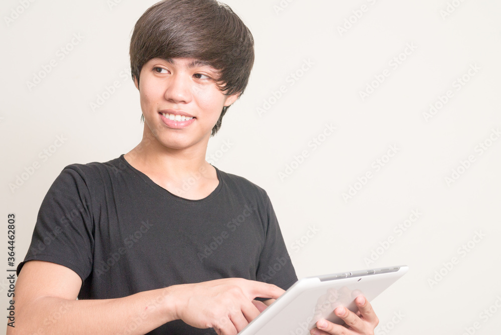 Portrait of happy young Filipino man thinking and using digital tablet Portrait of happy young Filipino man thinking and using digital tablet