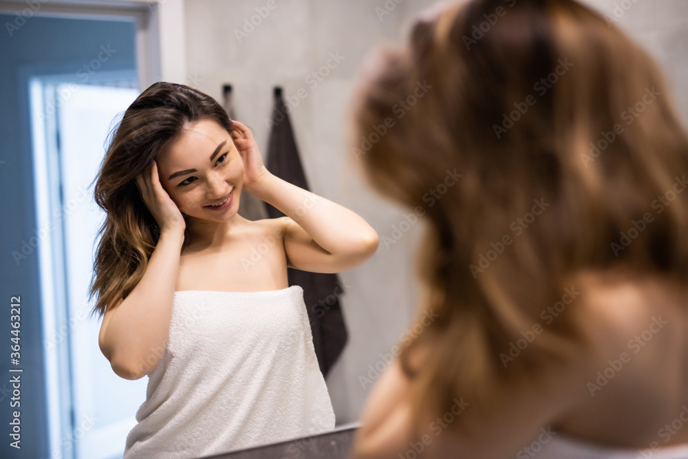 Young asian woman washing her face with water in the bathroom while looking herself in the mirror Young asian woman washing her face with water in the bathroom while looking herself in the mirror