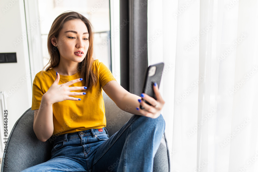 Young happy asian woman have online video chat using phone sitting in modern loft apartment Young happy asian woman have online video chat using phone sitting in modern loft apartment