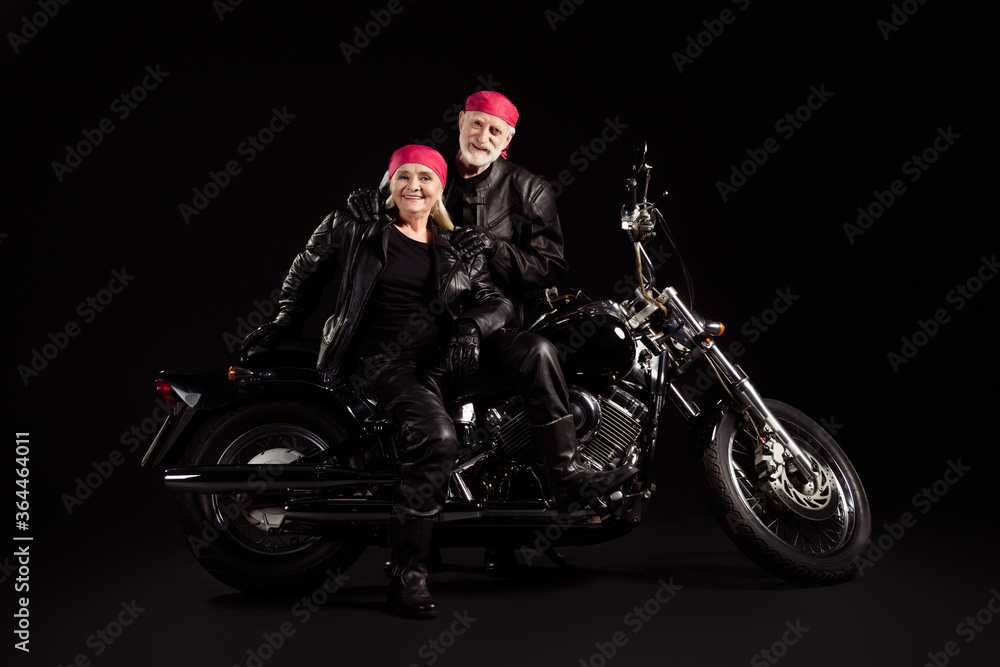 Photo of aged bikers grey haired man lady soulmates couple drive vintage chopper feel young metal music festival wear rocker leather jacket pants bandana isolated black color background