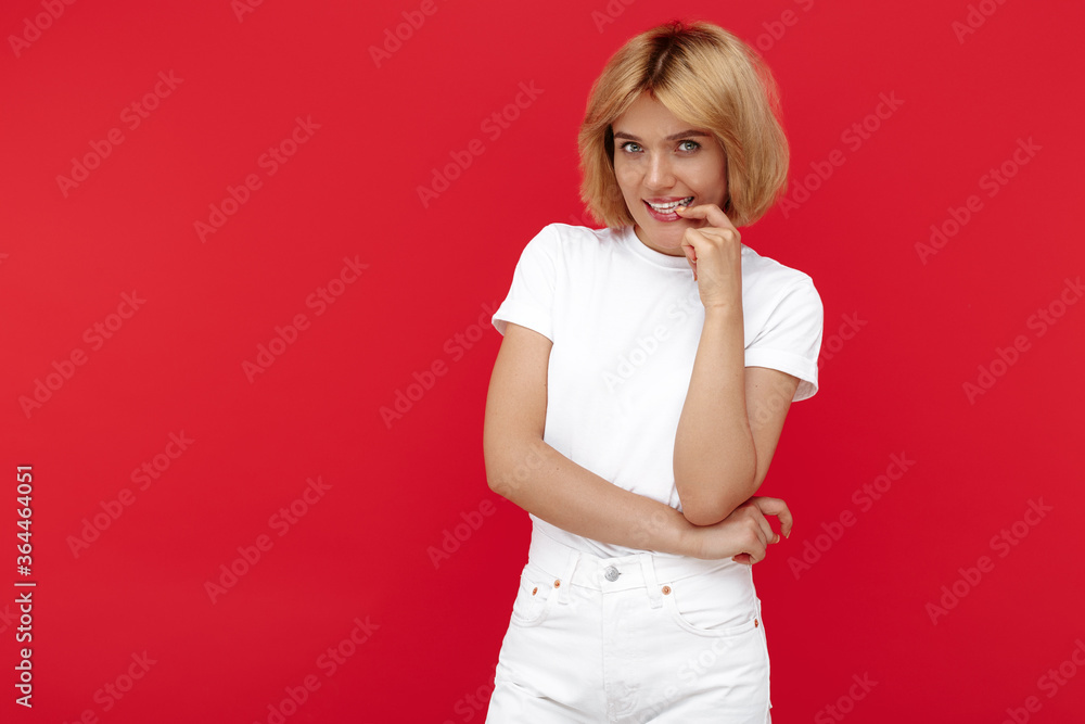 Timid young blonde woman in casual white outfit standing over red background. Timid young blonde woman in casual white outfit standing over red background.