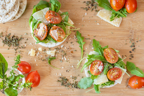 Angri, Italy. Food image of rice crackers snack with tomatoes, rocket salad, parmisan flakes, oregano and olive oil, on a wooden cutting board. Italian food ingredients.