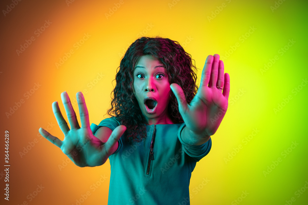 Shocked rejecting, stopping. African-american young woman's portrait on gradient background in neon. Beautiful female model. Concept of cinema, emotions, facial expression, sales, ad. Copyspace. Shocked rejecting, stopping. African-american young woman's portrait on gradient background in neon. Beautiful female model. Concept of cinema, emotions, facial expression, sales, ad. Copyspace.