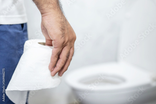 Man suffers from diarrhea hand hold tissue paper roll in front of toilet bowl. constipation in bathroom. Treatment stomach pain and Hygiene, health care concept.
