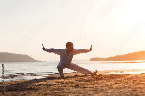 man praticing tai chi chuan at sunset on the beach. Chinese management skill Qi's energy. solo outdoor activities. Social Distancing 
 photo