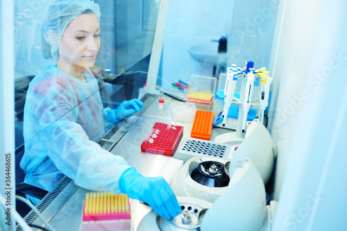 A young female scientist works in a sterile genetic or bacteriological laboratory with a dispenser and reagents in a medical gown  gloves and a doctor s cap.