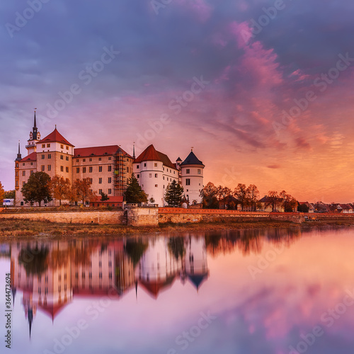 Wonderful sunrise view of Schloss Hartenfels, with colorful sky reflected in Elbe river . Picturesque morning view of castle on banks of the Elbe. Torgau. Saxony, Germany. creative Scenic image.