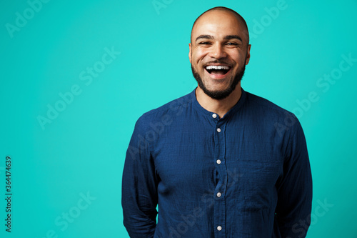 Joyful dark-skinned man laughing against turquoise background