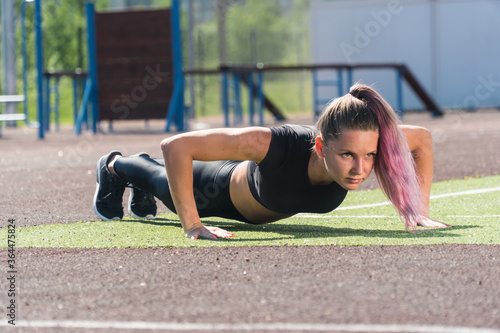 The girl on the mat does outdoor exercise. Exercise to stand in a bar, pushing a woman in the park