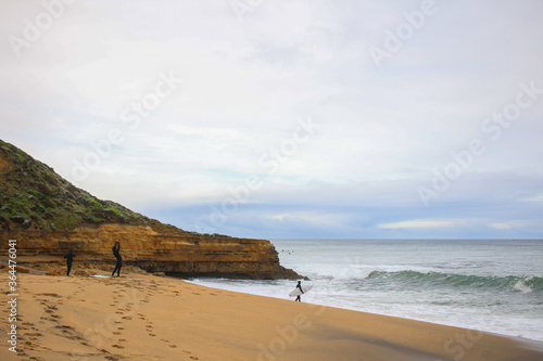 a group of unidentifiable surfers in wetsuits preparing themselves to join the surf off the rocky coastline of the great ocean road, Victoria, Australia