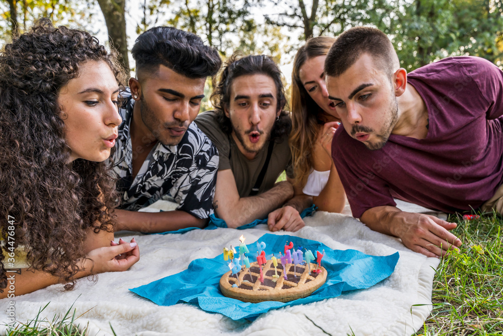 multiethnic group of millennial friends celebrating a birthday with a cake outdoors multiethnic group of millennial friends celebrating a birthday with a cake outdoors