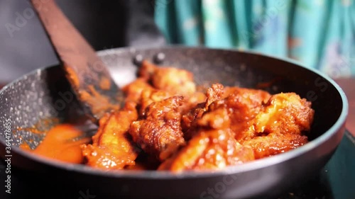 Closeup of hot and spicy buffalo chicken wings being stirred in a non-stick pan