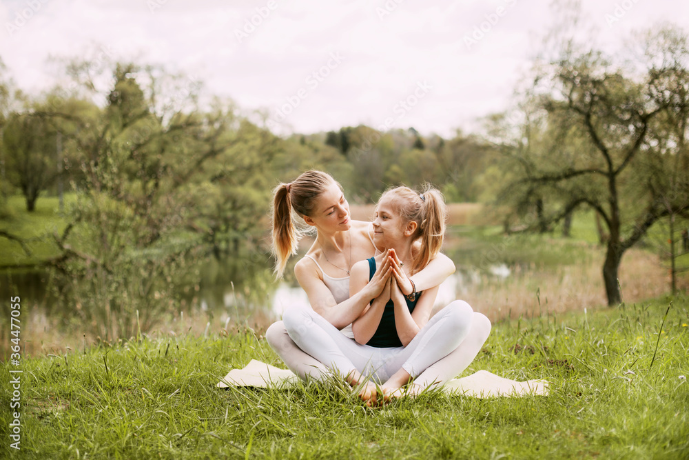A young mother and daughter in sportswear do yoga together in a Park. The concept of a family holiday. Sports, fitness, meditation A young mother and daughter in sportswear do yoga together in a Park. The concept of a family holiday. Sports, fitness, meditation
