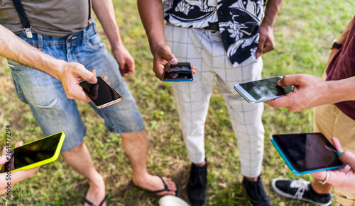 group of multiracial friends in a public park outdoors using smartphones