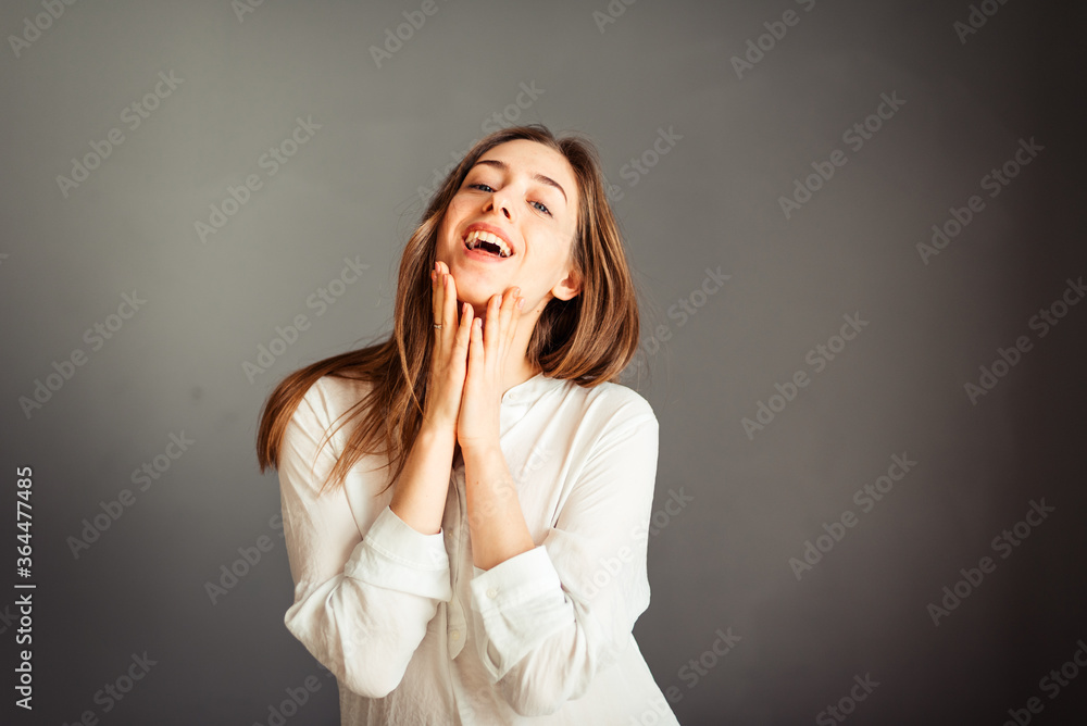 Young girl in a white shirt, hands up, on a gray background. Honest and emotional on the banner, billboard, billboard. No retouch. Without make-up. Young girl in a white shirt, hands up, on a gray background. Honest and emotional on the banner, billboard, billboard. No retouch. Without make-up.