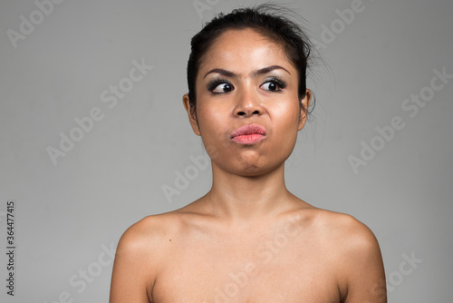 Face of shirtless Asian woman thinking and looking disgusted