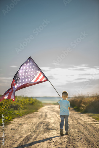 Child is holding American flag, back view.